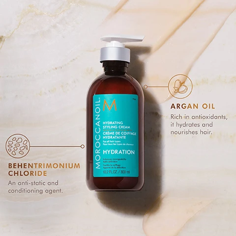 Image 3 - A brown bottle of Moroccanoil Hydrating Styling Cream with a turquoise label, featuring graphics describing argan oil and behentrimonium chloride, placed on a light marble surface.
Image 4 - A side-by-side comparison of a woman’s hair before and after a styling treatment, with BEFORE above the left image and AFTER above the right image, showing a transition from frizzy, untamed hair to sleek, shiny hair.
Image 5 - A hand holds a bottle of Moroccanoil Hydrating Styling Cream, which has a turquoise label, with the text made with argan oil to promote hydrated hair and an anti-static agent to help fight frizz.
Image 7 - Three square graphics on a marble background stating that products are free from sulfates, phosphates, and parabens, certified cruelty-free by PETA, and made from 100% post-consumer recycled materials.