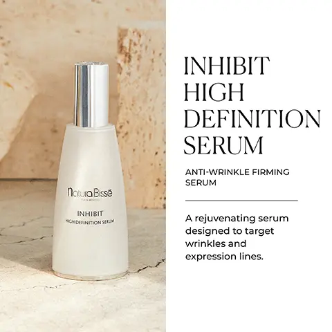 Image 1 - A bottle of Natura Bissé Inhibit High Definition Serum is displayed on a light textured surface, with visible text reading Inhibit High Definition Serum, Anti-Wrinkle Firming Serum, and a description stating a rejuvenating serum designed to target wrinkles and expression lines.
Image 2 - A white bottle of Natura Bissé Inhibit High Definition Serum is placed beside a textured cream stone, with icons and text highlighting key benefits: relaxes, replenishes, lifts, rejuvenates.
Image 3 - A smiling woman with long brown hair wearing a light beige top is shown in a bright interior, accompanied by text that reads A SCIENTIFIC MASTERPIECE, followed by a description about a formula with rejuvenating ingredients and icons indicating gluten free, alcohol free, and suitable for vegans.
Image 4 - A clear container with a gel-like substance inside, with text on the right that describes various ingredients and their benefits: SCIENCE BEHIND IT OCTAMOXYL® & RELAXTRIPEPTYL Helps relax the appearance of expression lines. COPPER & COLLAGEN PEPTIDES Provides a lifting and tightening effect. DERMAFILL COMPLEX-III Hyaluronic acid and moisturizing ingredients, such as Aquaxyl and niacinamide, contribute to a plump, supple complexion. MATRIXYL A potent firming peptide that targets sagging and provides a lifting effect.
Image 5 - A collection of skincare products displayed on a light background, including bottles and jars labeled Natura Bissé, with the text at the top reading AT-HOME WRINKLE REMEDY and a description below it about a revolutionary skincare concept.