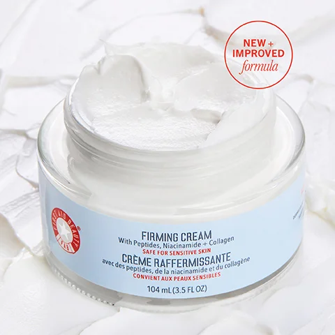 A jar of firming cream with a smooth white texture is partially open, surrounded by cream and bearing a label that states FIRMING CREAM With Peptides, Niacinamide + Collagen SAFE FOR SENSITIVE SKIN and NEW + IMPROVED formula.