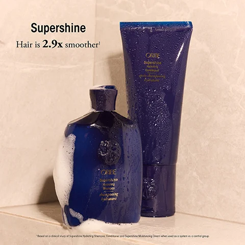 Two Oribe Supershine hair products, a bottle and a tube, shown with water droplets and foam spilling from the bottle, with text Supershine Hair is 2.9x smoother¹ ORIBE Supershine Hydrating Shampoo shampooing hydratant ORIBE Supershine Hydrating Conditioner apres-shampooing hydratant ¹ Based on a clinical study of Supershine Hydrating Shampoo, Conditioner and Supershine Moisturizing Cream when used as a system vs. a control group.