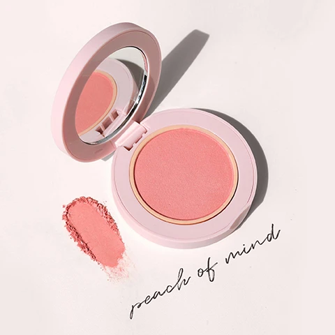 Image 1 - A pink blush compact with a mirror, showing a soft pink powder, placed next to a swatch of the blush, with the text peach of mind below it.
Image 2 - Three women with various skin tones and hairstyles smile in a collage, featuring close-up portraits and a bottom right corner swatch of blush with the text peach of mind soft peachy-pink.
Image 3 - A round container of a pink cosmetic powder is shown, with text listing key ingredients: Hyaluronic Acid replenishes and maintains moisture, Squalane smooths, softens, and hydrates skin, Aloe Leaf Extract calms visible redness and soothes inflammation, Jojoba Esters moisturize and soften skin, and an explanation of Soft Sphere Liposomal Technology for effective absorption.
