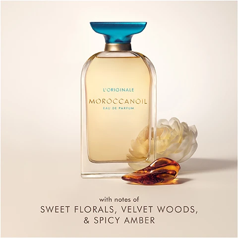 Image 1 - A bottle of Moroccanoil Eau de Parfum is displayed with a light-colored background, featuring a teal cap and a floral accent beside it, along with the text with notes of sweet florals, velvet woods, and spicy amber.
Image 2 - A clear bottle of Moroccan oil perfume with a turquoise cap sits on a rock near water, with the text INSPIRED BY THE MEDITERRANEAN displayed above.
Image 3 - A woman with curly hair is looking directly at the camera while seated near the water, with the text WHERE WILL IT TAKE YOU? and LORIGINALE EAU DE PARFUM displayed at the bottom.
Image 4 - Three bottles of Moroccanoil perfume are displayed on a light background, with the sizes labeled as 10 ml, 60 ml, and 100 ml.
Image 5 - A woman with curly hair holds a perfume bottle near her face, wearing a black sleeveless top, with a colorful tiled background, and visible text reads ADRIA ARJONA for Moroccanoil.