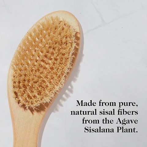 Image 2 - A close-up of a dry body brush with a light wood handle and tan bristles, on a white marble surface, next to the text Made from pure, natural sisal fibers from the Agave Sisalana Plant. Image 3 - A long-handled dry brush with light-colored bristles and a rope loop on the handle, with the word goop visible on the handle, is shown in the bottom right of a white textured background, alongside the text: G.Tox Ultimate Dry Brush, Benefit 1 Sweeps away dead skin cells. Benefit 2 Wakes up your whole body. Benefit 3 Leaves skin silky-smooth. Image 4 - A person with dark skin is shown with crossed legs and one hand resting on an ankle, against a light grey background, with the text: Exfoliate, wake up your senses, and just feel good all over. Image 5 - A wooden body brush with natural bristles and the word goop debossed on its handle lies on a green and white striped towel, next to instructions that read How to Use It STEP 1: Brush skin before a bath or shower. STEP 2: Starting at your feet, gently brush upward toward your heart. STEP 3: Use firm, small strokes or work in a circular motion.